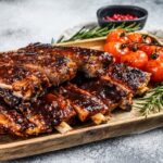 Delicious barbecued ribs seasoned with a spicy basting sauce and served with baked tomatoes. Gray background. Top view.