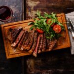Sliced grilled beef barbecue Striploin steak with arugula salad and Red wine on dark background
